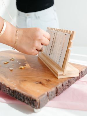 A hand uses a wooden jewelry holder on a rustic slab to organize accessories.