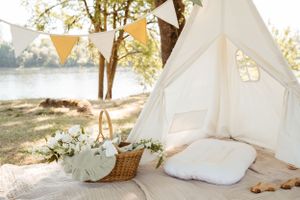 A dreamy outdoor setup with a white tent, pillows, and decorative bunting near water.