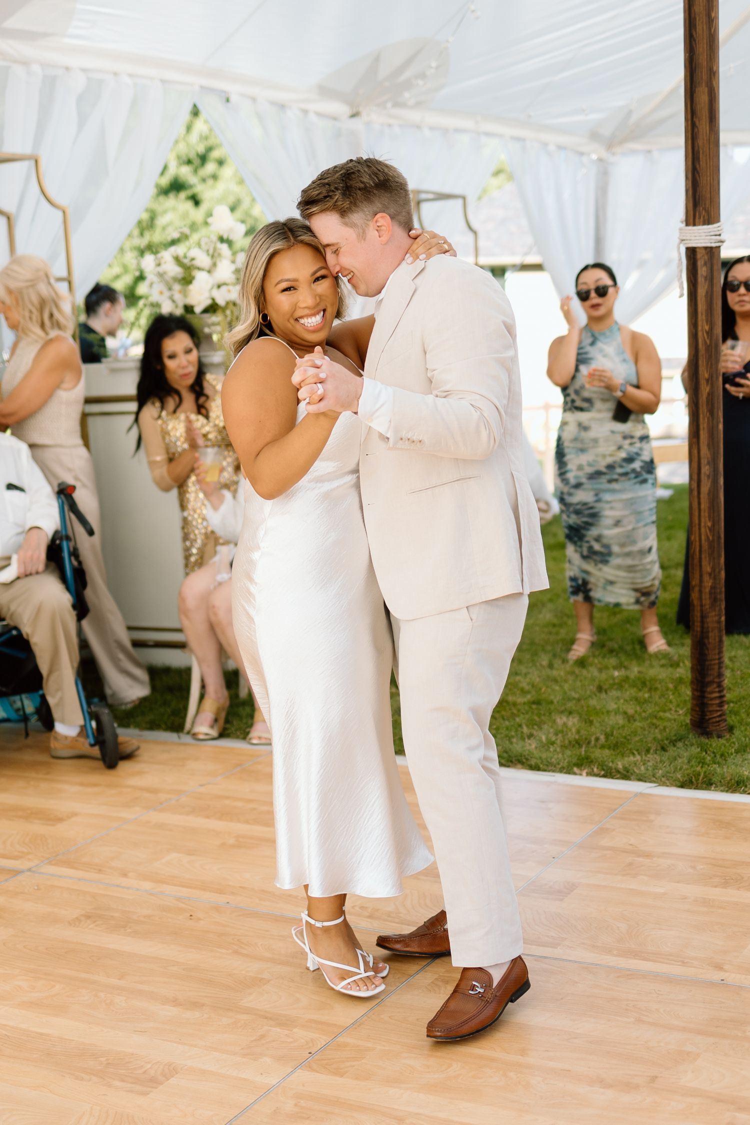A joyful couple dances together on a wooden floor under a white tent during their outdoor wedding celebration.