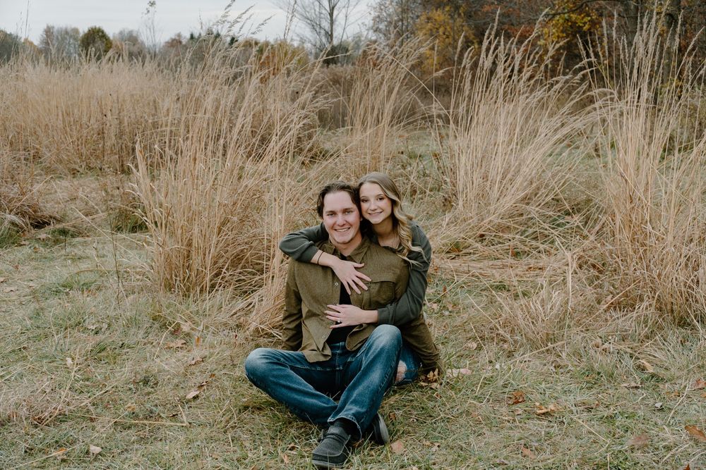A couple embraces while sitting in a field of dried autumn grass.