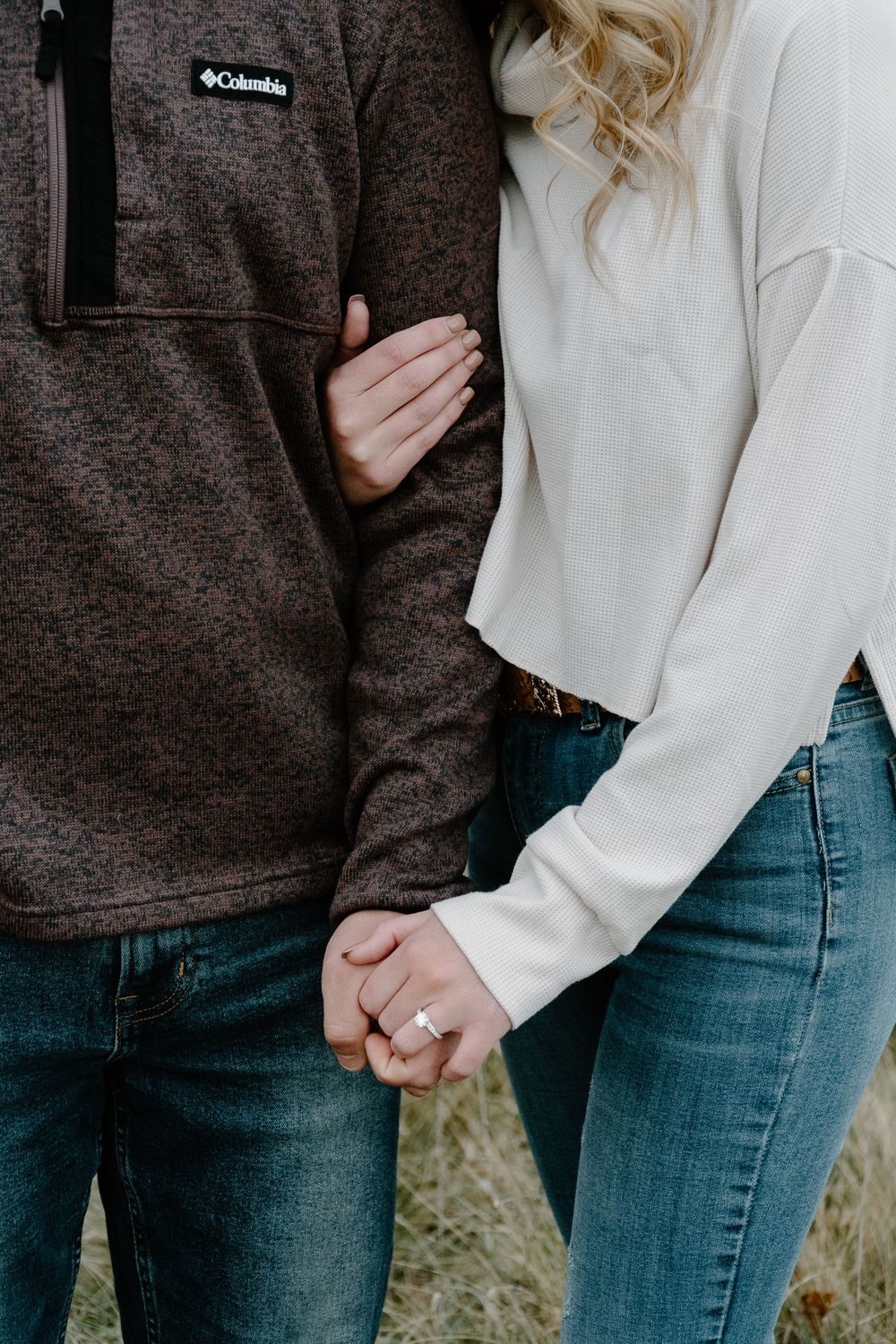 Close-up of a couple wearing Columbia fleece and white sweater showing engagement ring.