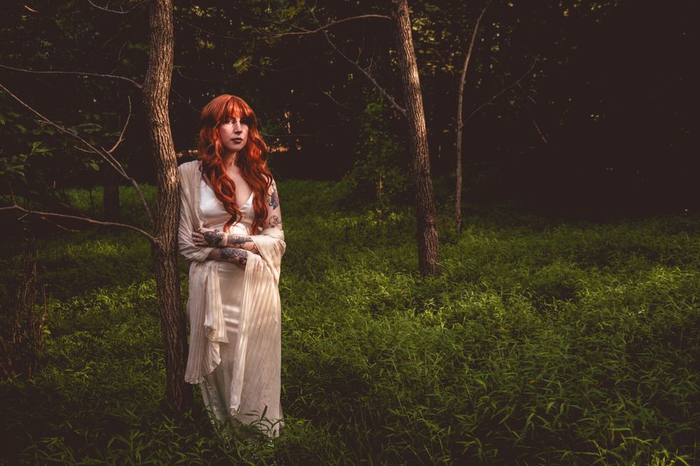 Romantic forest portrait featuring white dress against shadowy woodland.