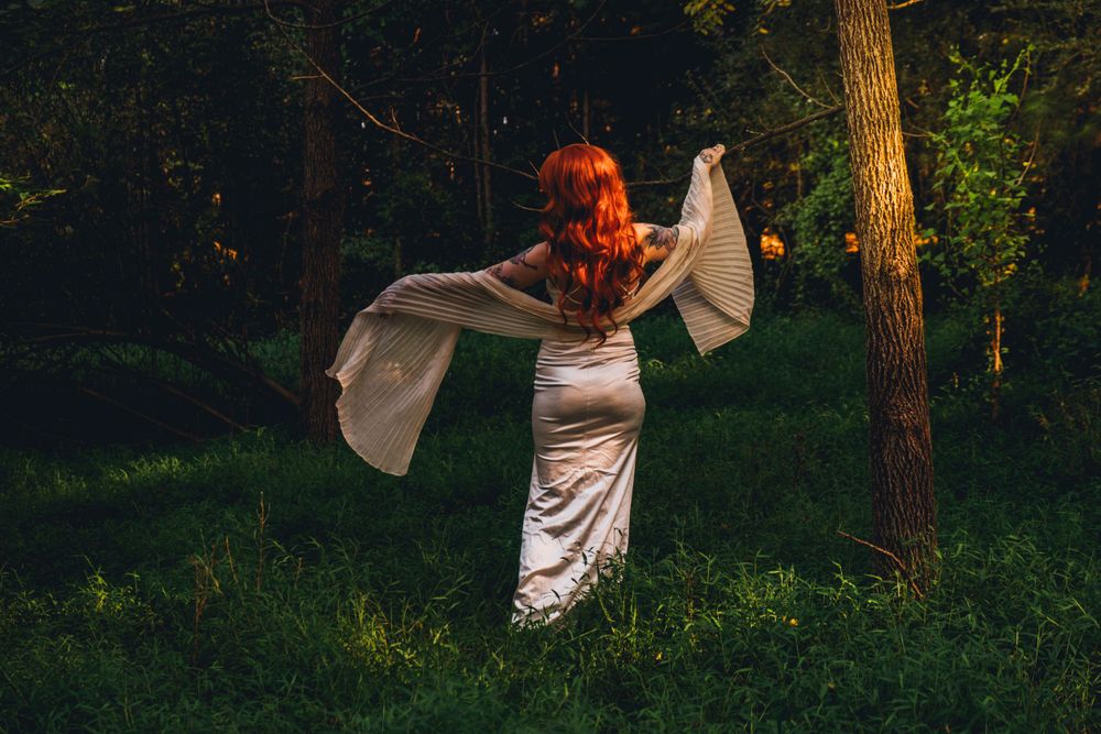 Figure in white dress twirls fabric in mystical forest setting.
