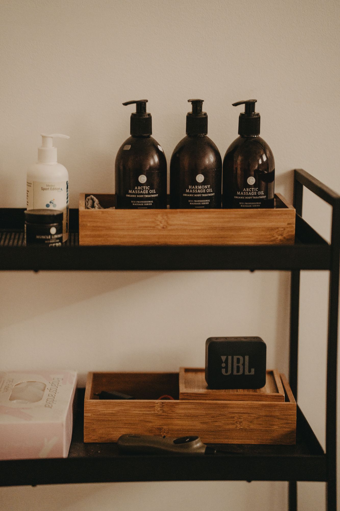 Black pump bottles and wooden organizers arranged on dark metal shelves with a small JBL speaker.