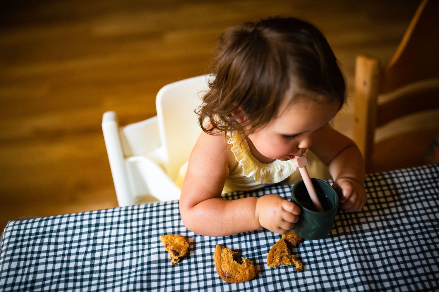 A child excitedly leans over an outdoor table to enjoy drinks through colorful straws in the sunshine.