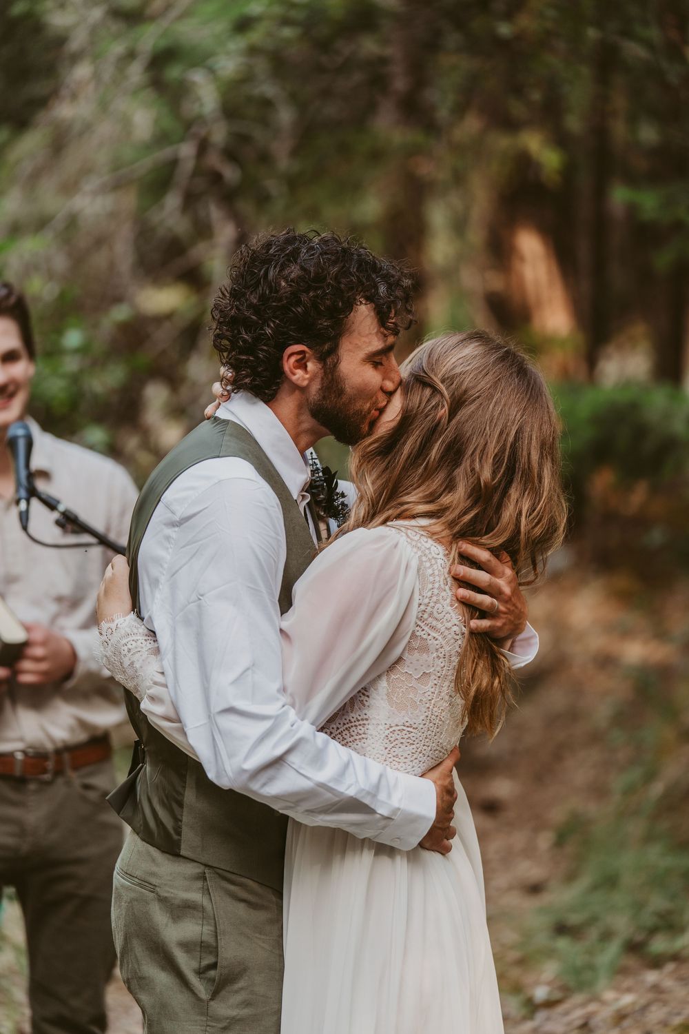 A romantic outdoor wedding moment showing a couple in white and earth tones embracing in a natural forest setting.