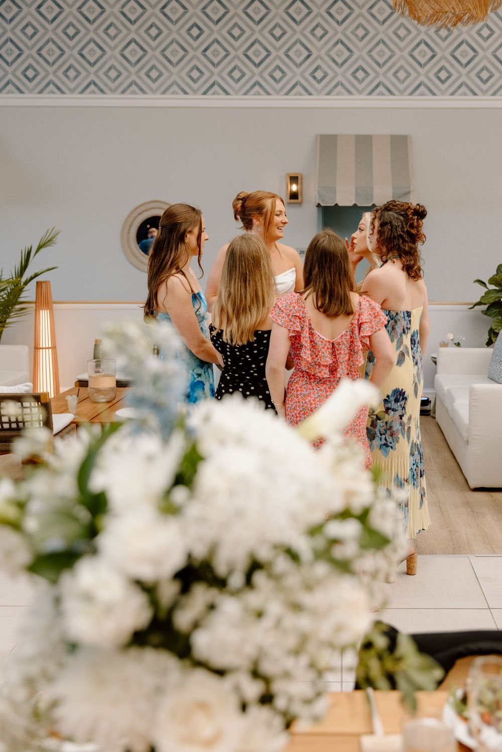 A group of people in floral dresses gather together at an elegant event with white floral decorations.