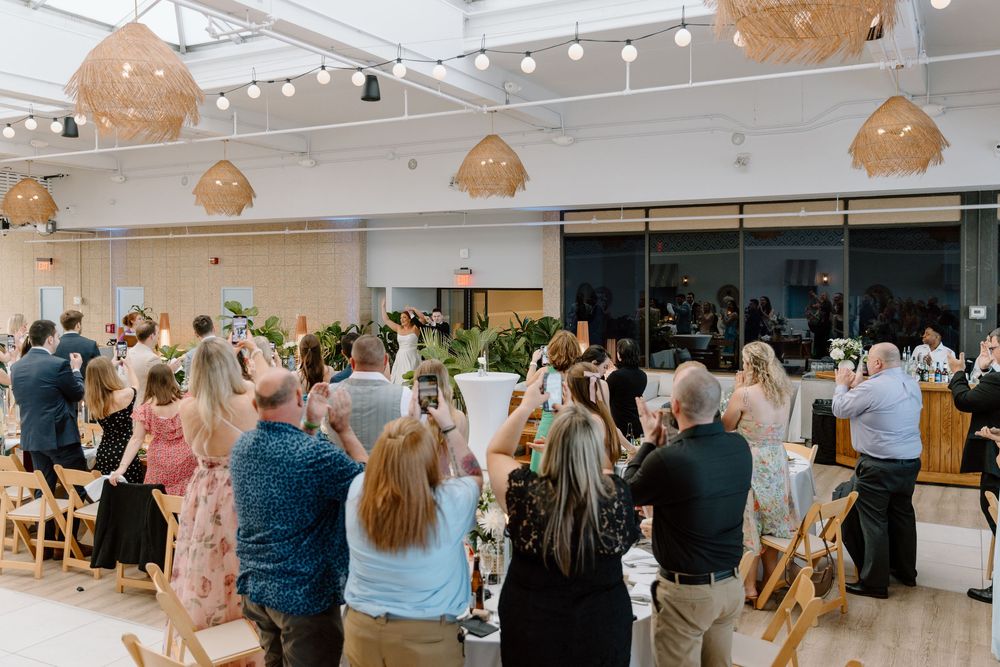 Wedding guests seated in an elegant venue with warm lighting from woven pendant lamps overhead.