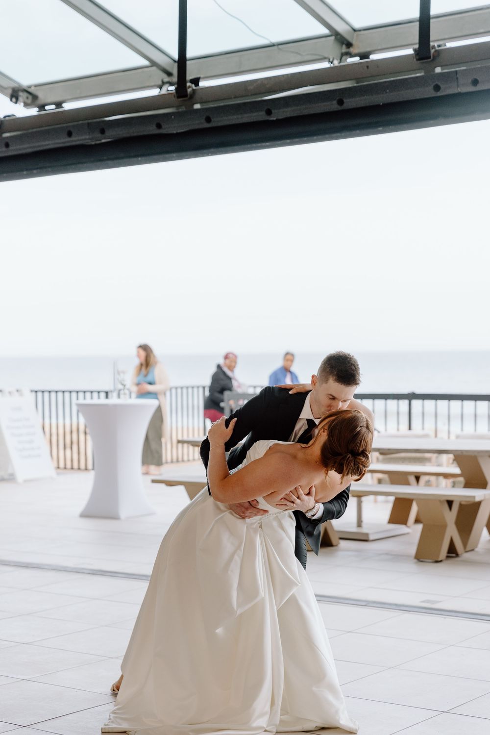 Couple dancing and embracing on an oceanfront terrace with cocktail tables and railing in background.