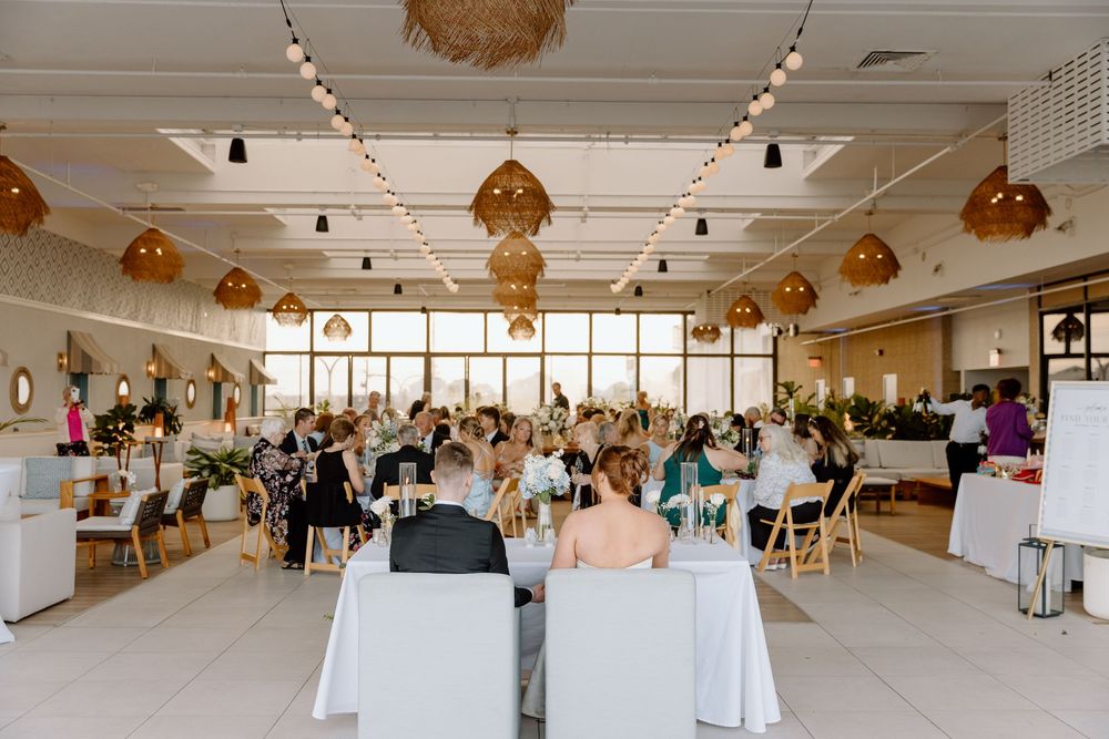 Large bright event space with rattan pendant lights and round tables set for a wedding reception.