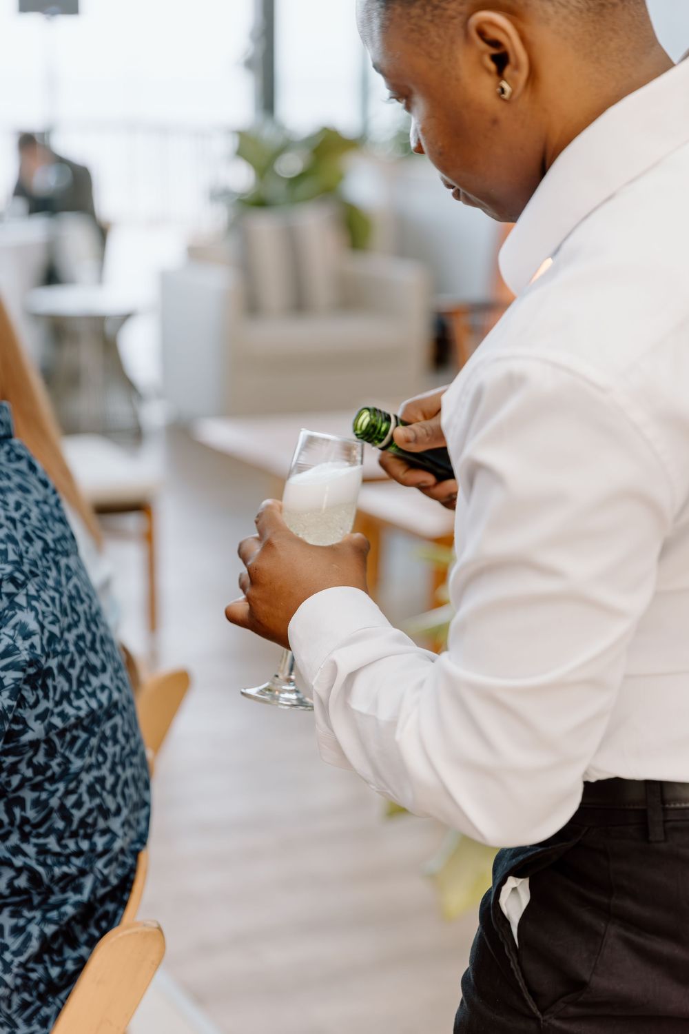 A server in formal attire pours champagne into a glass at an upscale restaurant.