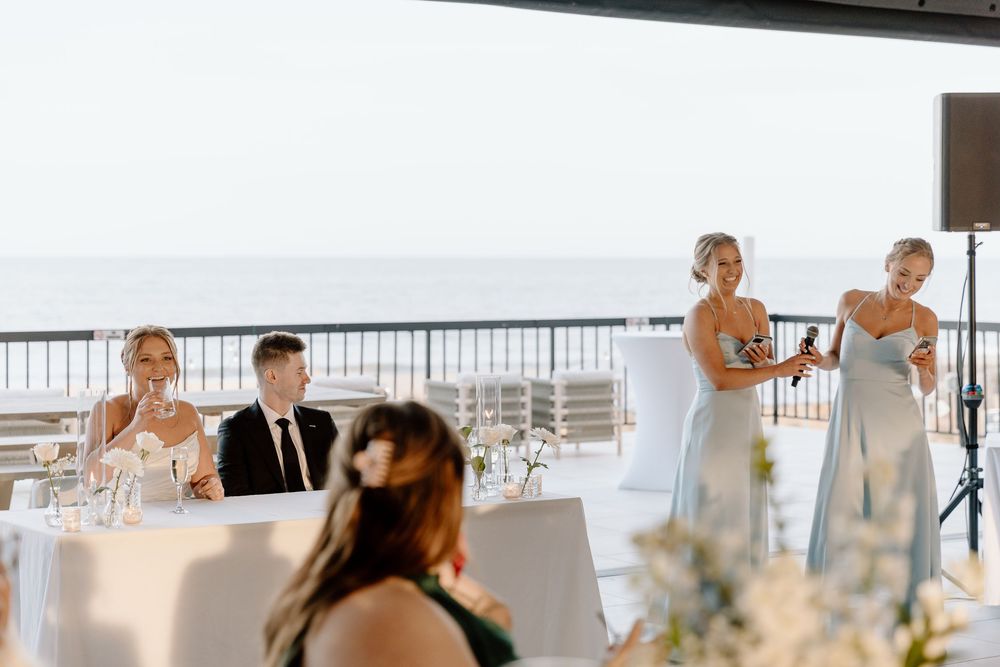 Wedding reception setup with white tables and ocean view through large windows.