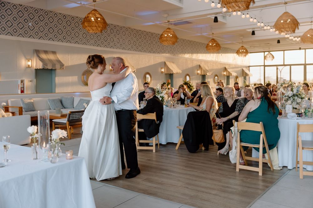 Large banquet hall with ornate gold pendant lights and geometric wallpaper during a wedding celebration.