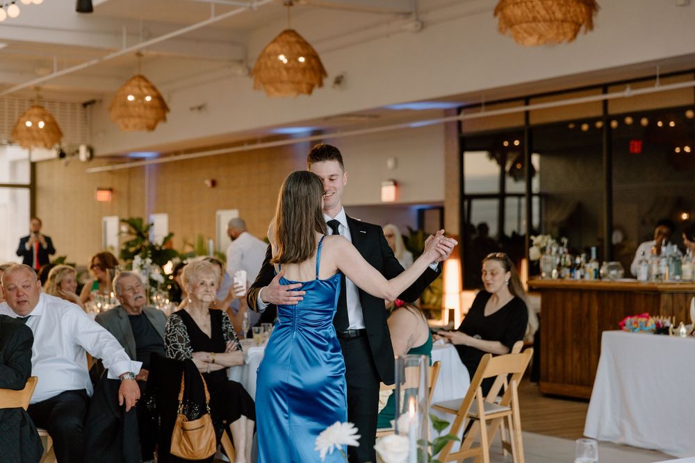 A couple dances together during a wedding reception as guests watch under warm pendant lighting in an elegant venue.