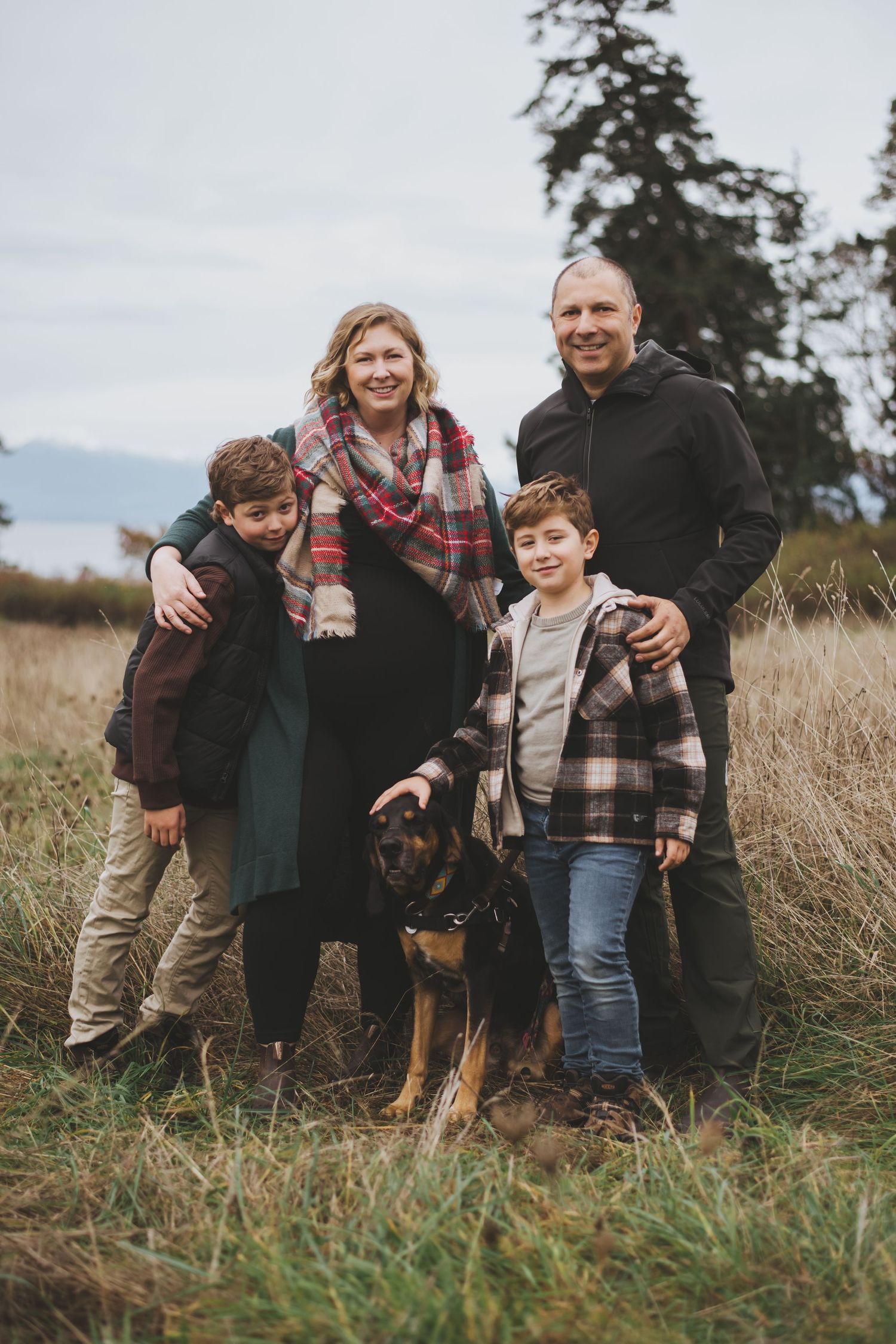 A family and their dog pose together in a grassy field on an overcast autumn day.