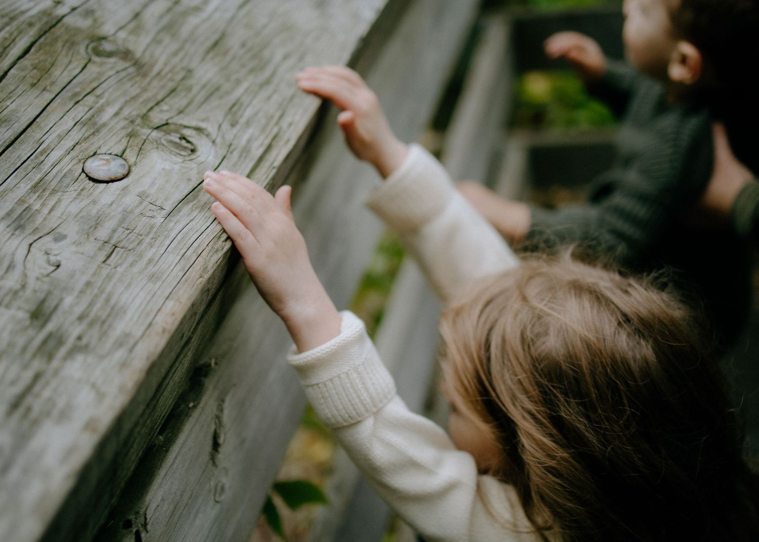 Small hands reach up to touch a weathered wooden surface.