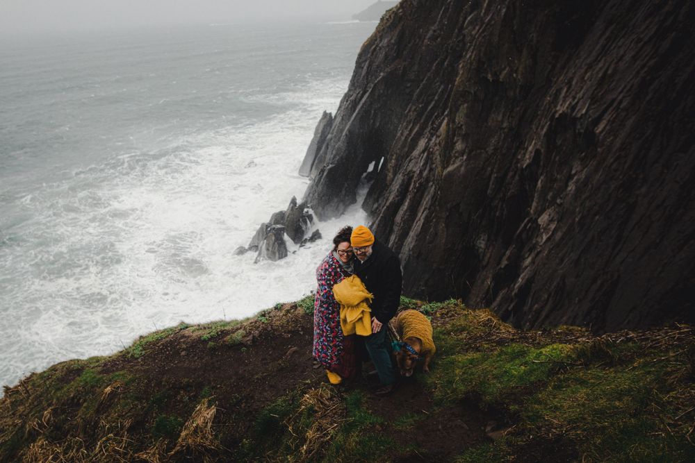 People in bright yellow jackets explore a steep coastal cliff above crashing ocean waves.