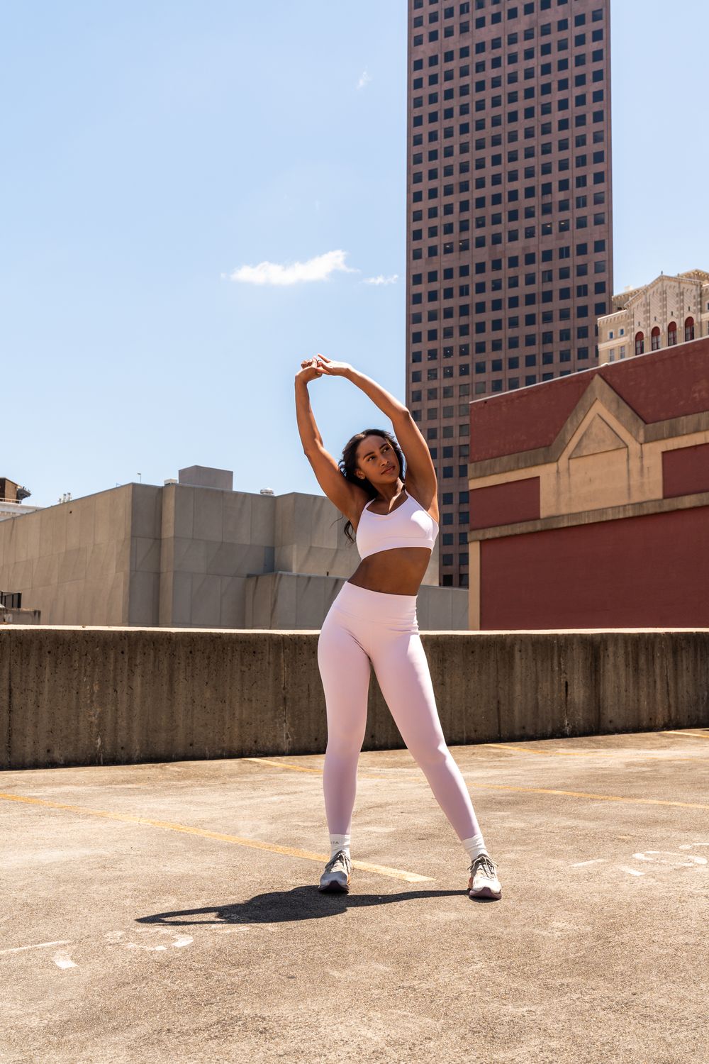 Woman in matching pink workout set performing stretching exercise on rooftop.
