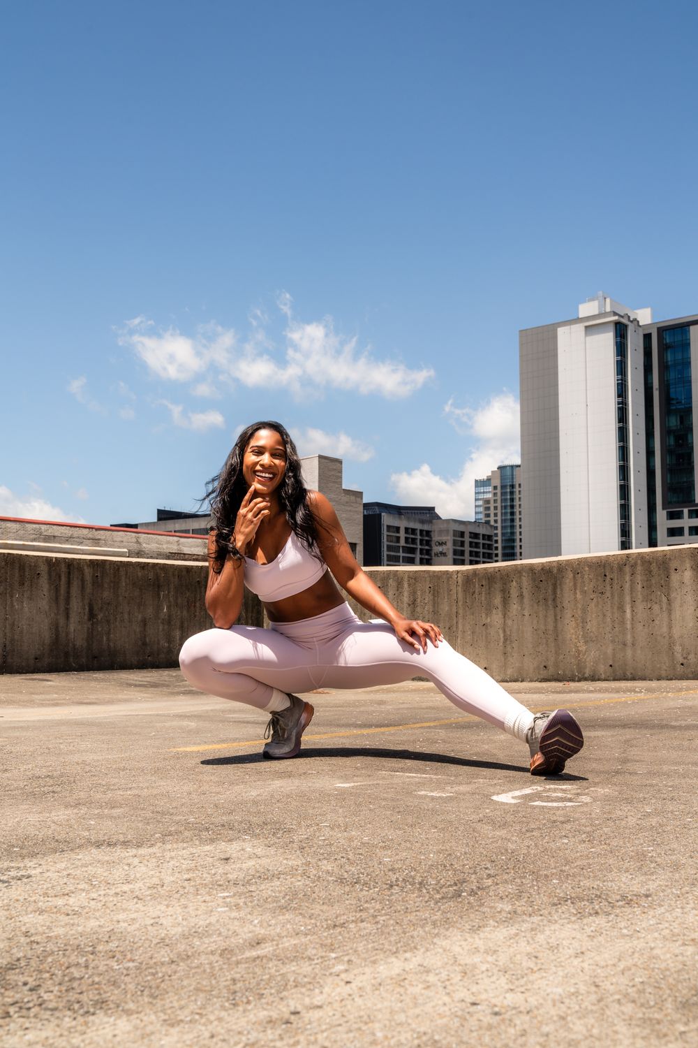 Woman in pink athletic wear performs deep squat exercise on urban rooftop.