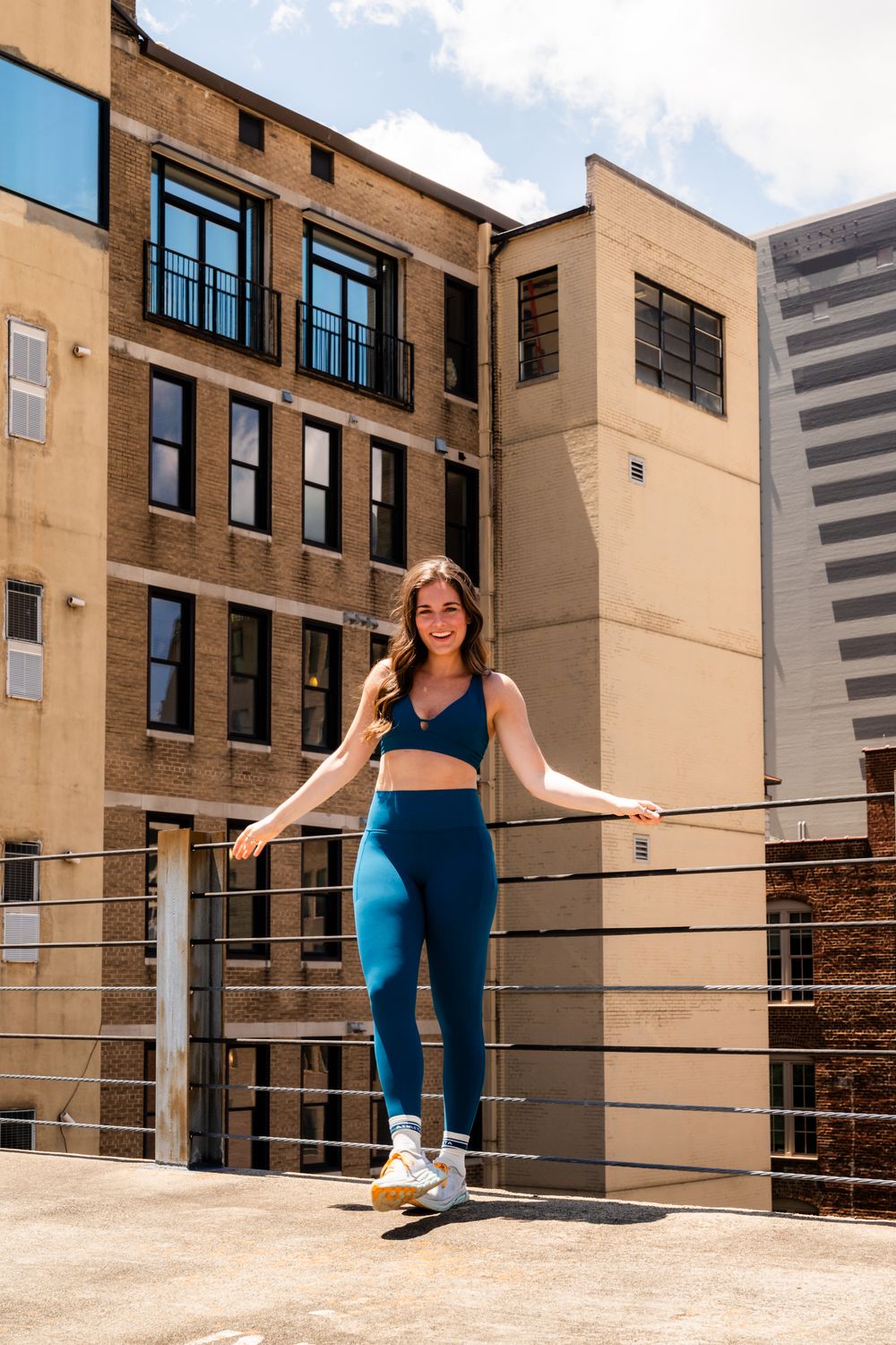 Woman in blue athletic wear practicing balance exercises on a rooftop ledge.
