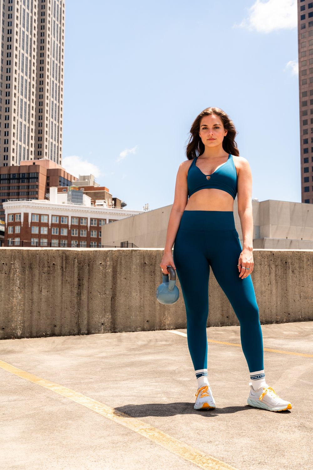 Woman in blue athletic wear poses during rooftop workout with city buildings in background.