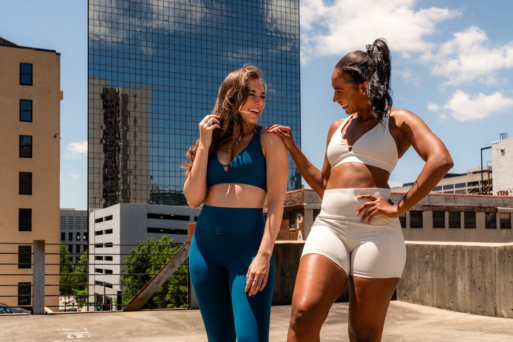 Athletic duo in contrasting blue and white workout sets having animated conversation on urban rooftop.