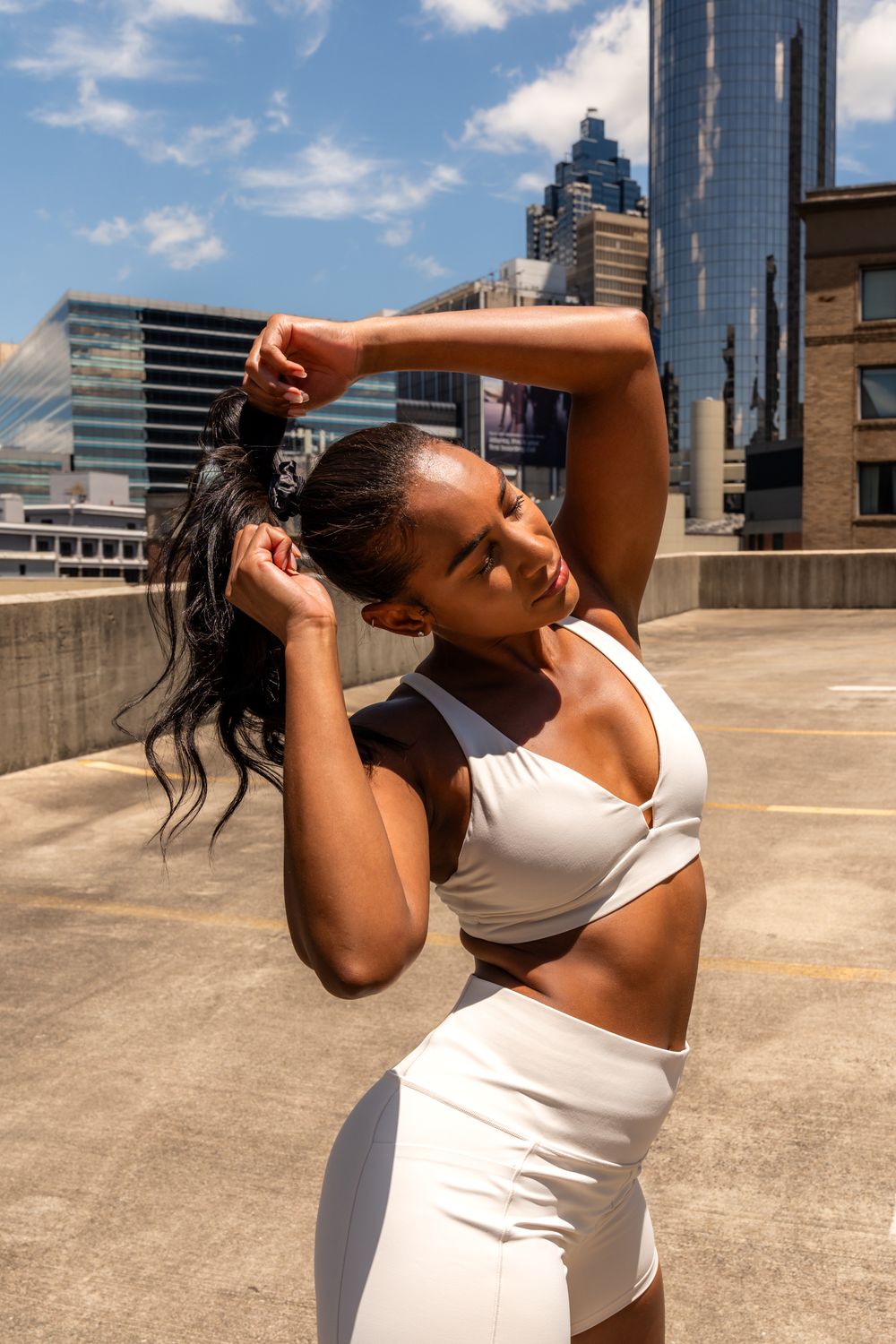 Woman in white athletic set stretching gracefully against cityscape background.