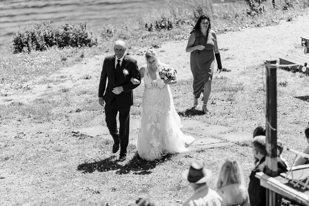 A couple walks together with guests on a grassy outdoor path during a fall wedding celebration.
