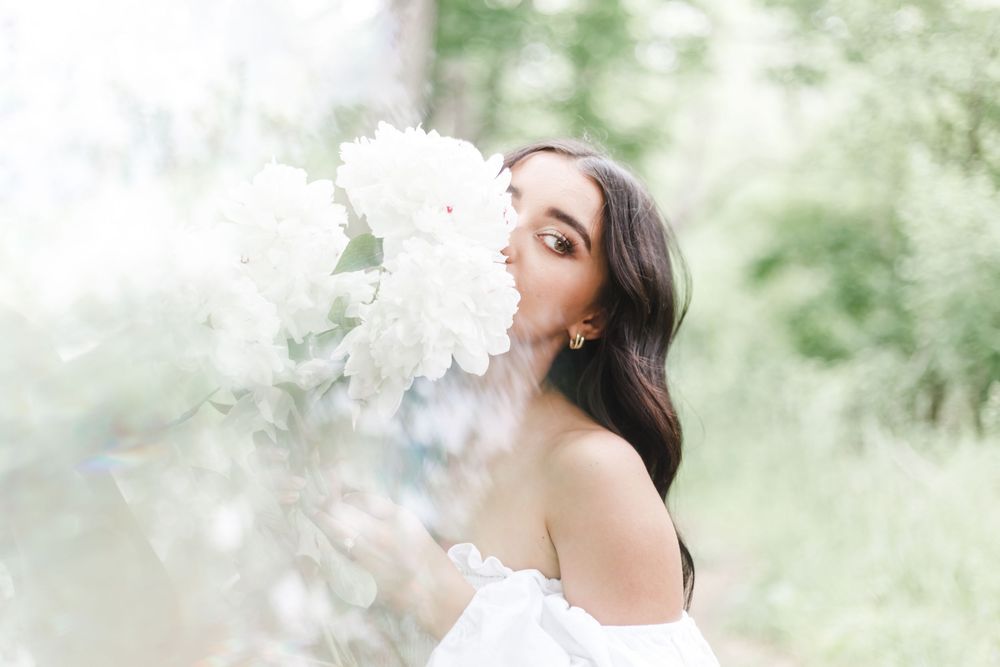 Artistic portrait with soft smoke effects and white floral elements against a sunlit natural backdrop.