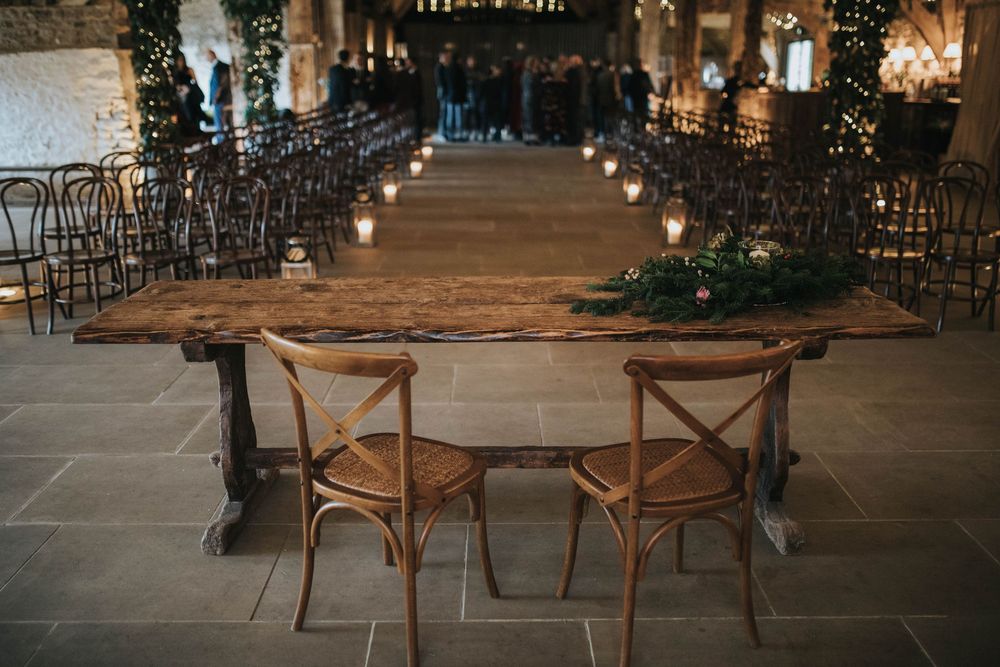 Rustic wooden cross-back chairs line up in neat rows during an evening wedding ceremony setup with twinkle lights.