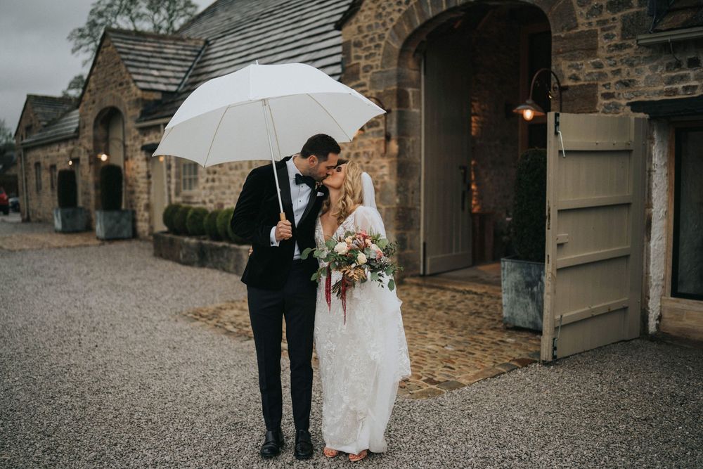 Couple in formal wedding attire entering rustic stone building with vintage wooden doors.