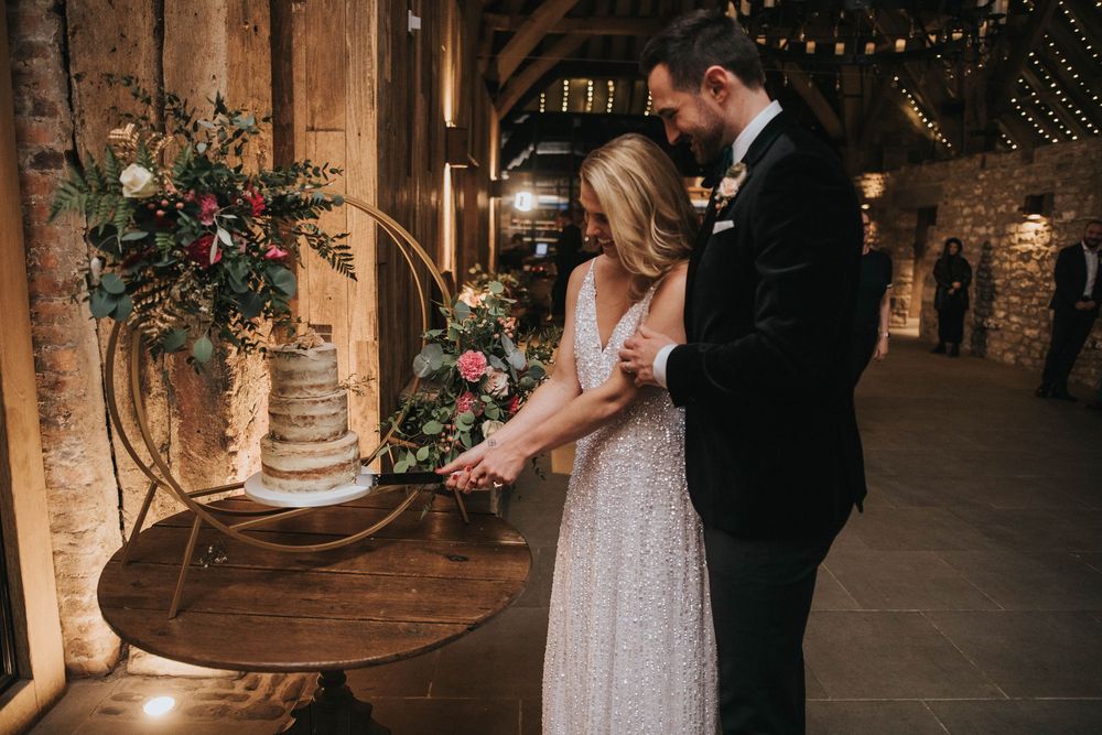 A couple shares a tender moment in a rustic barn wedding venue with string lights and floral arrangements.