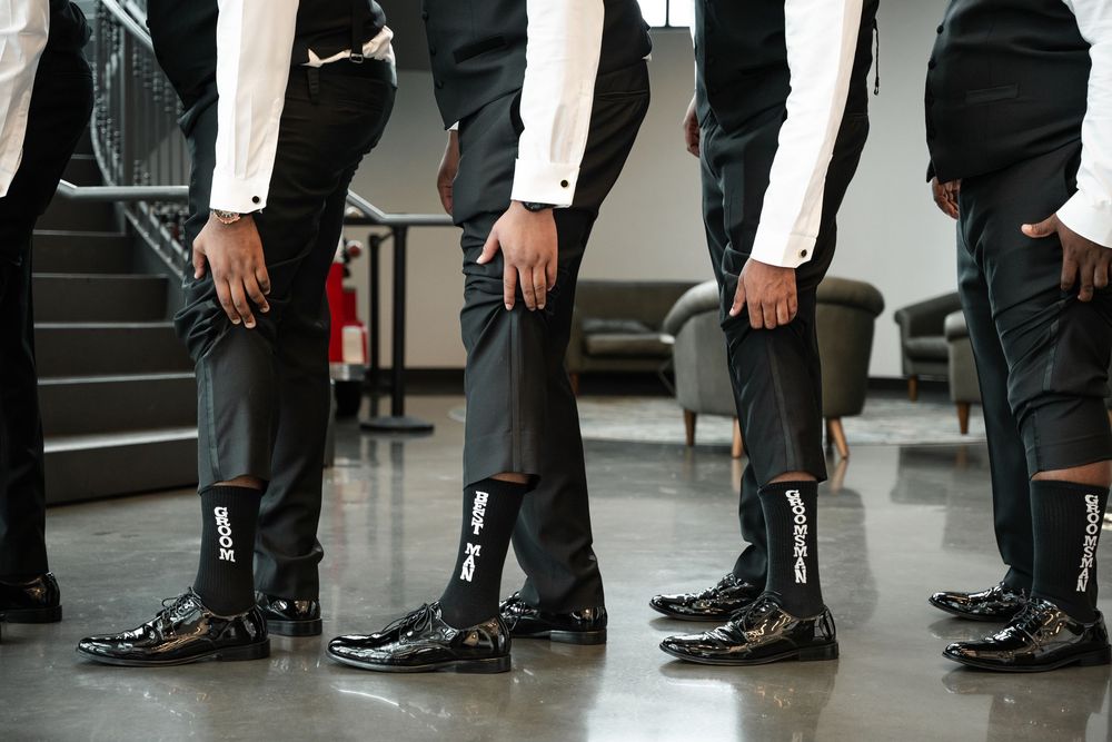 Several pairs of formal black dress shoes and pants are shown lined up in a row on a light colored floor.