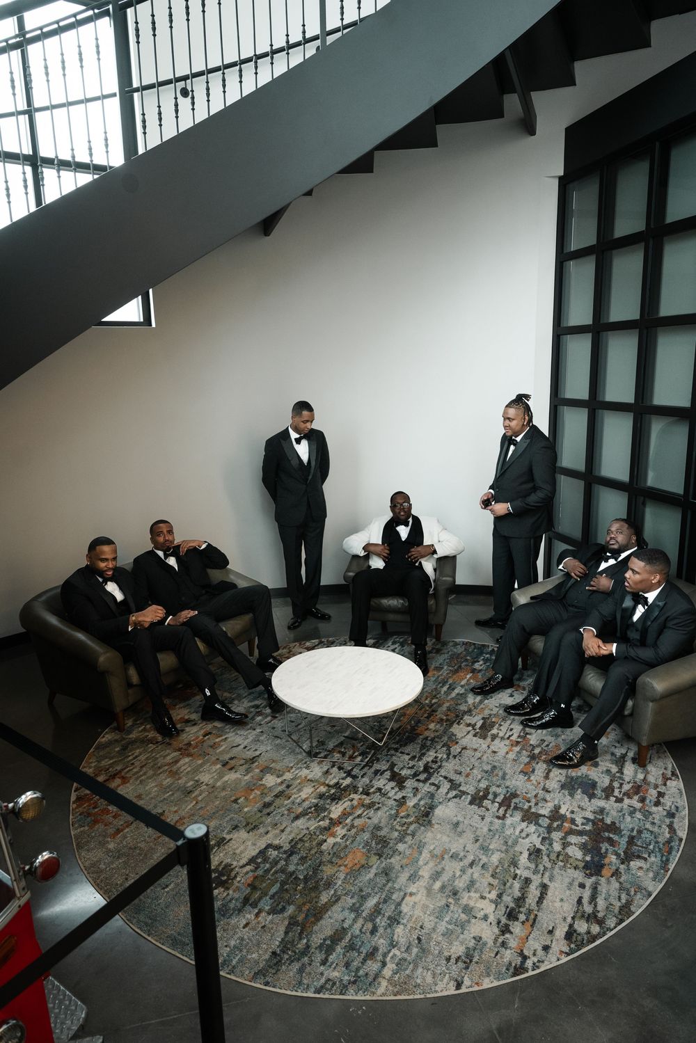 A group in formal attire sits casually in a modern space with white walls and a patterned circular rug.
