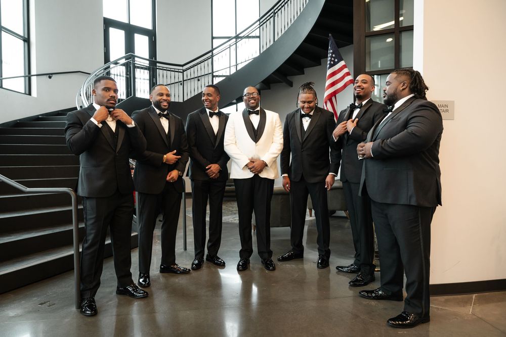 Groomsmen in formal black suits and ties line a staircase during a wedding celebration.