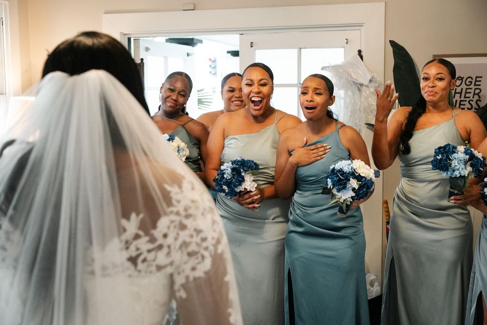 Bridesmaids in matching blue gowns laugh and embrace during a candid wedding moment.
