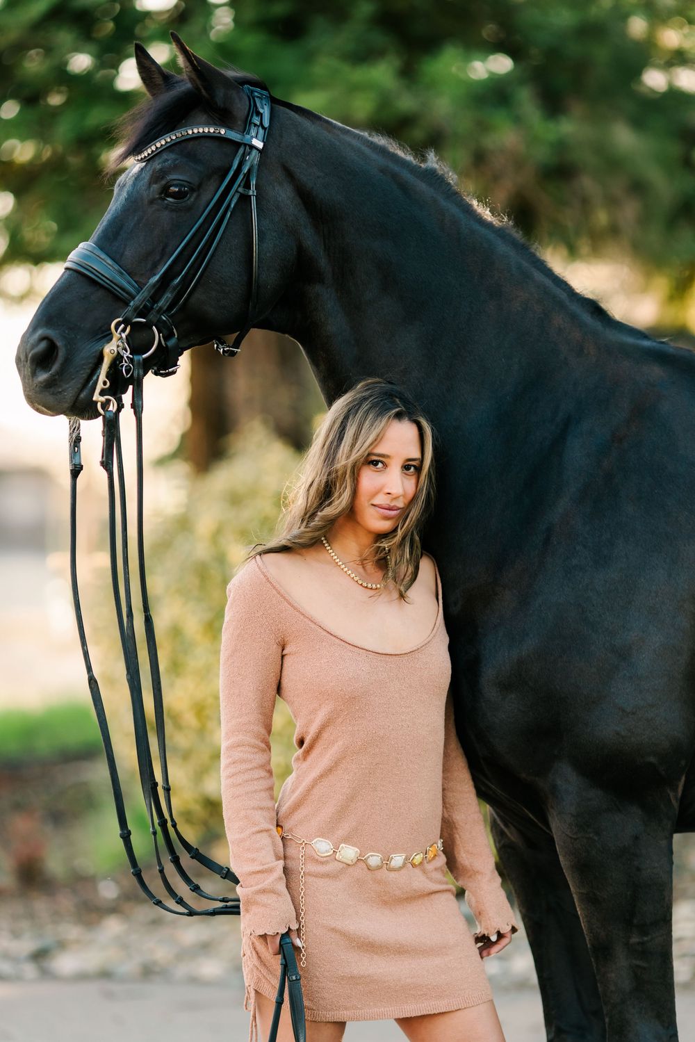 A majestic black horse and someone in a peach-colored sweater pose together during golden hour.