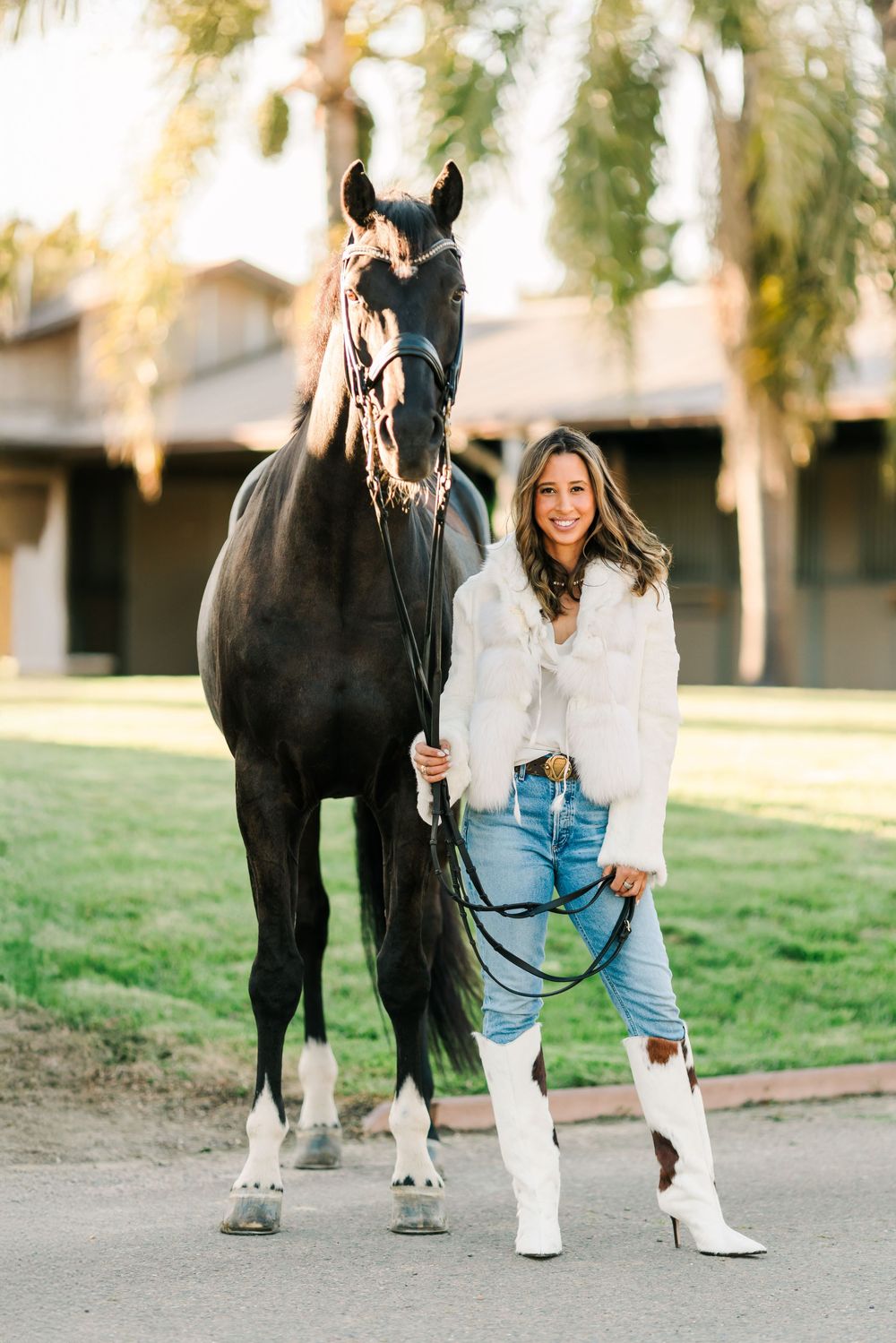 A dark horse stands beside someone wearing white boots and jeans on a grassy field.