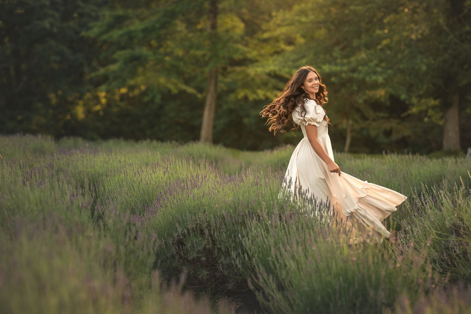 A person in a flowing white dress twirls gracefully in a serene lavender field as early evening light glows behind them.