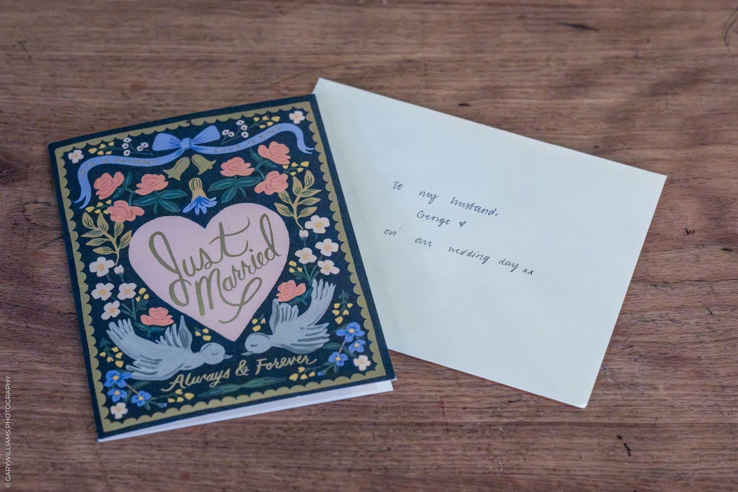 A collection of blue and pink wedding thank you cards with floral designs arranged on a rustic wooden table surface.