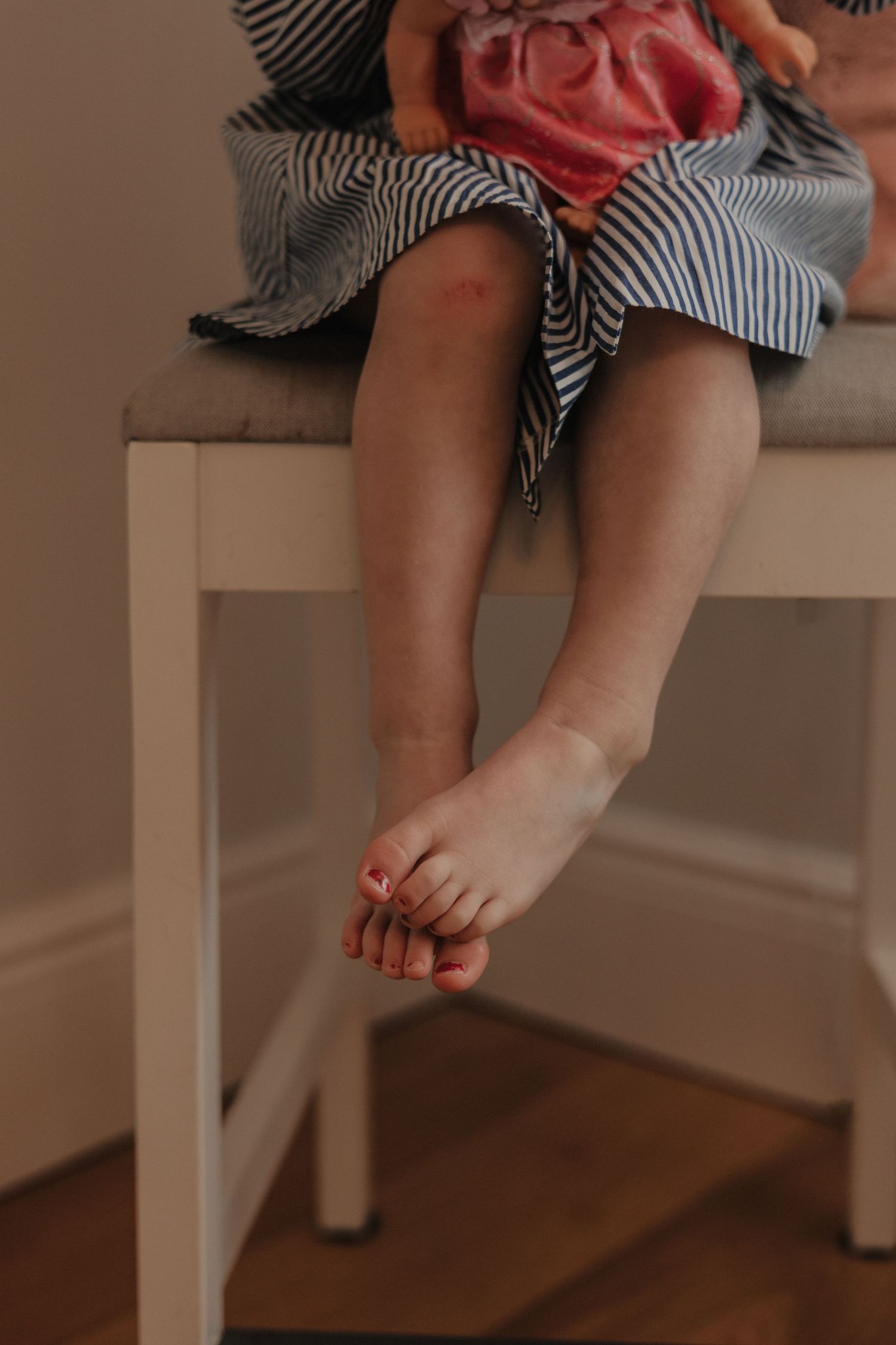close up toddler sitting on chair, legs hanging,scuffed know ,painted toes, colour,natural ,light