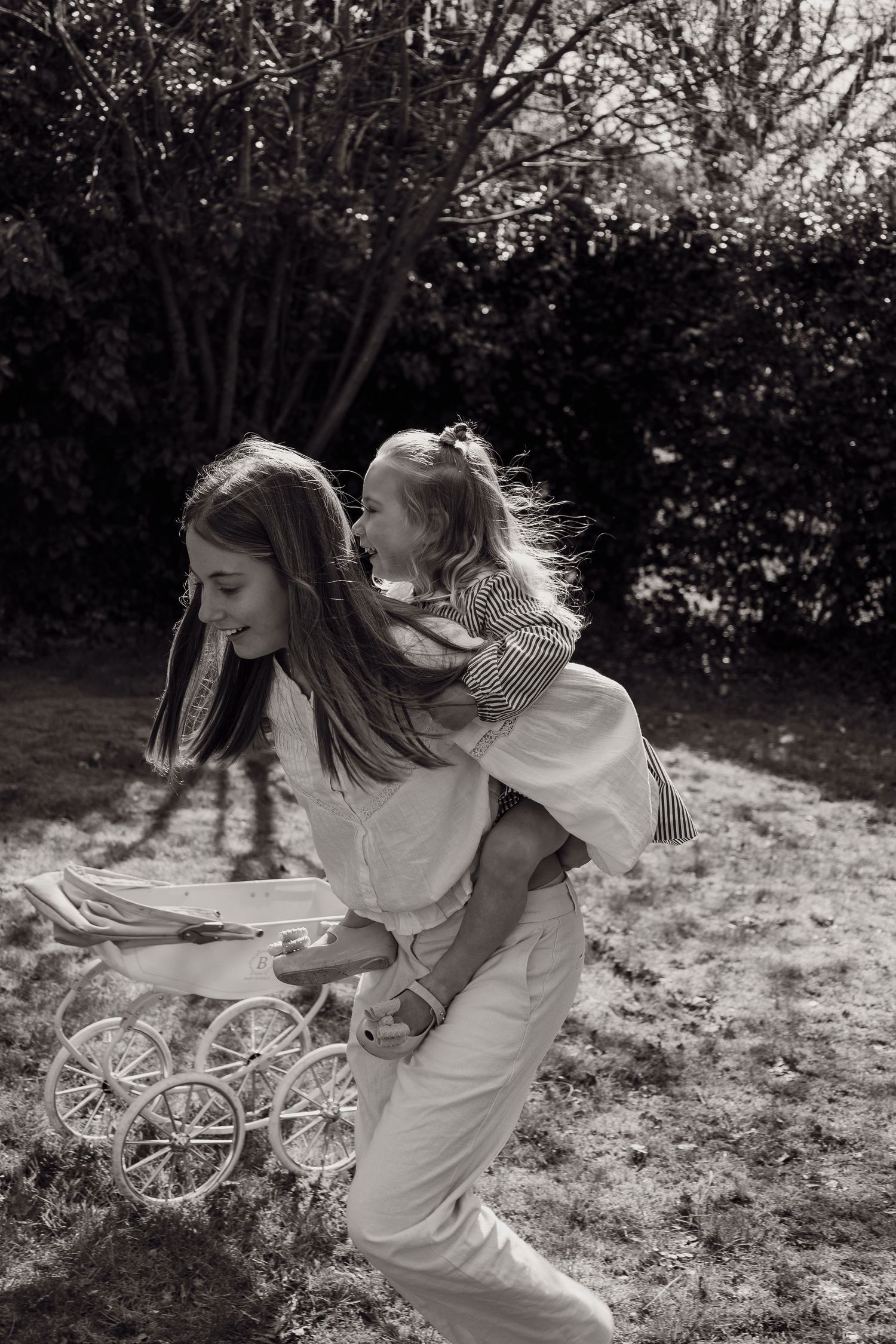 big and little sister piggyback running in grade, grainy, natural light, monochrome