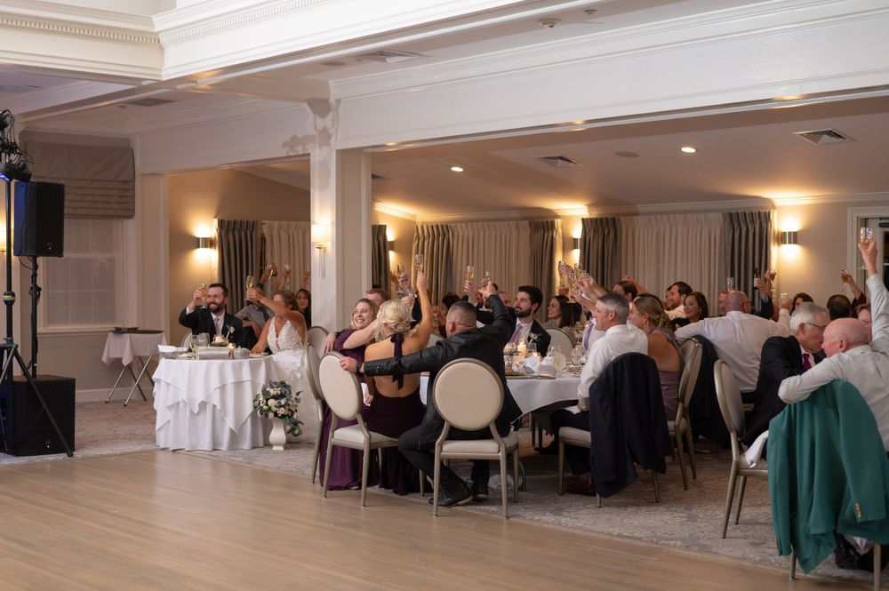 Wedding reception guests seated at elegant round tables in a bright ballroom with warm lighting and white decor.