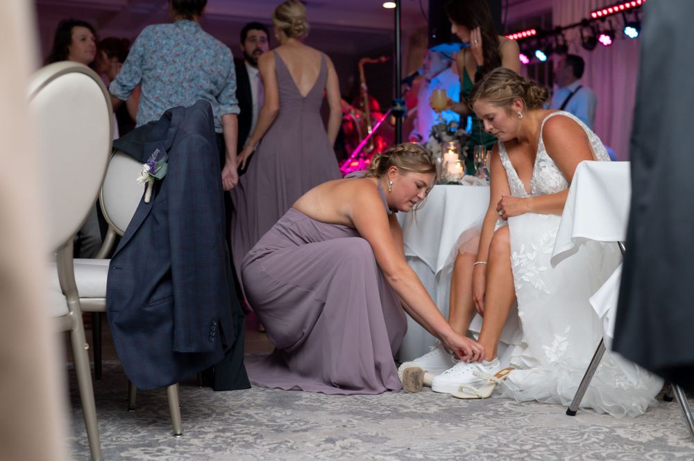 Someone helps adjust a wedding dress while others gather at a wedding reception.