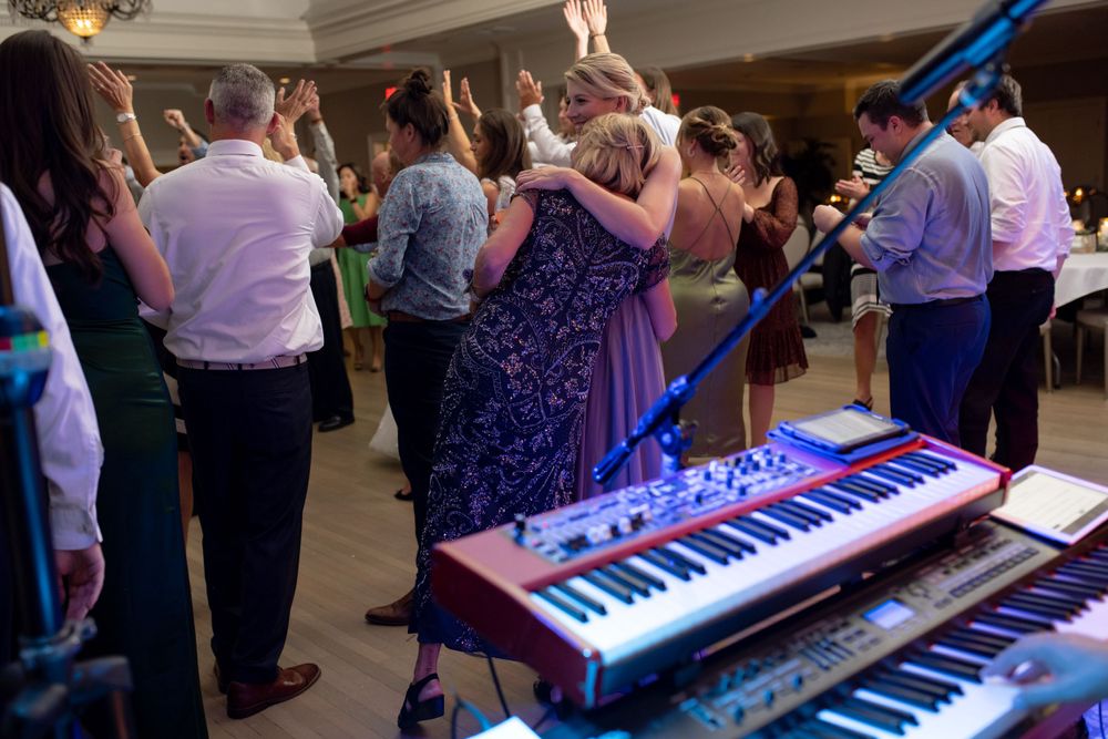 Wedding guests dance next to a keyboard setup at an indoor reception venue.
