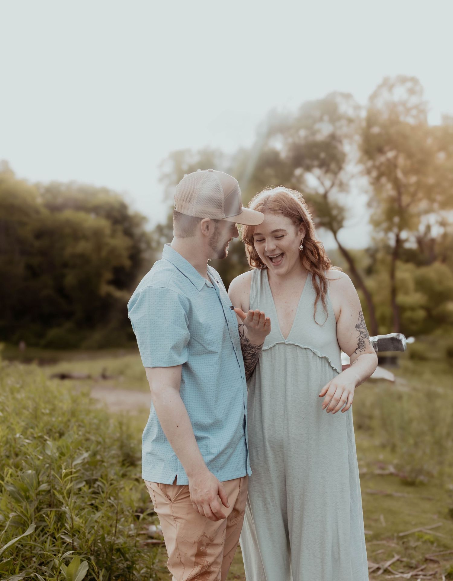 A couple shares a joyful moment together in a sunlit meadow during golden hour, dressed in casual summer attire.