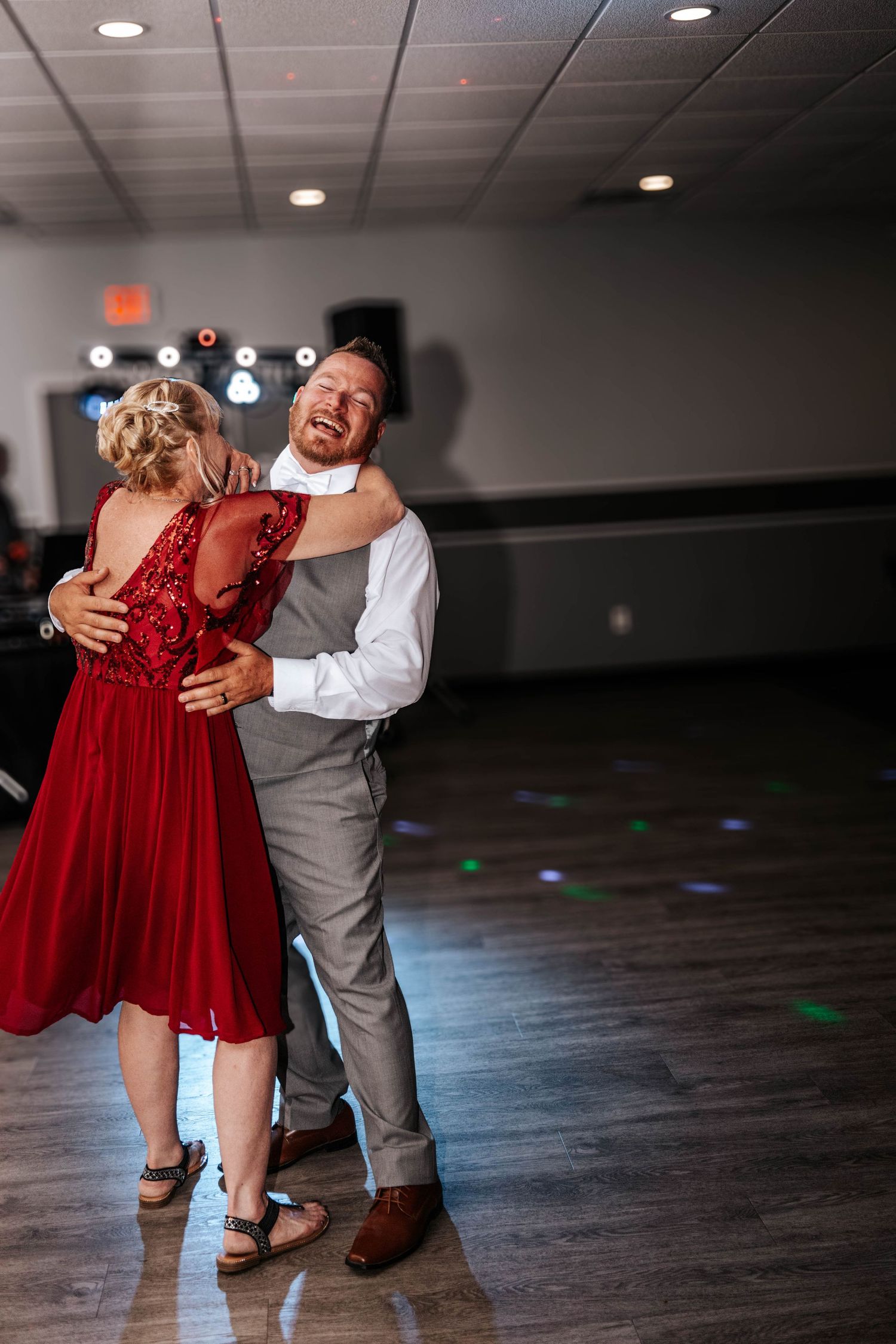 A couple dancing on a dark dance floor with sparkling lights, the woman wearing a red dress and the man in gray.