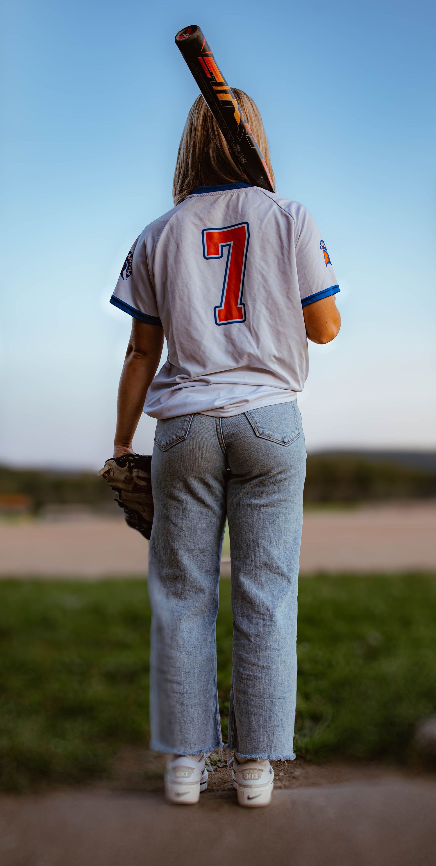 Back view of someone wearing baseball jersey with number 7 standing in grassy field at dusk.