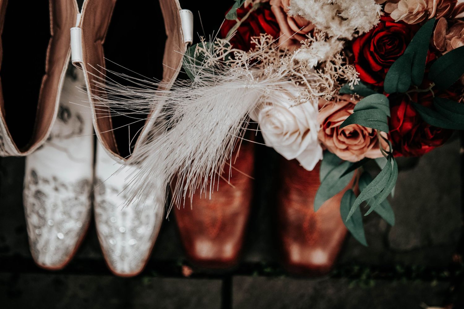 Elegant white lace wedding shoes with feathers and flowers in moody lighting.