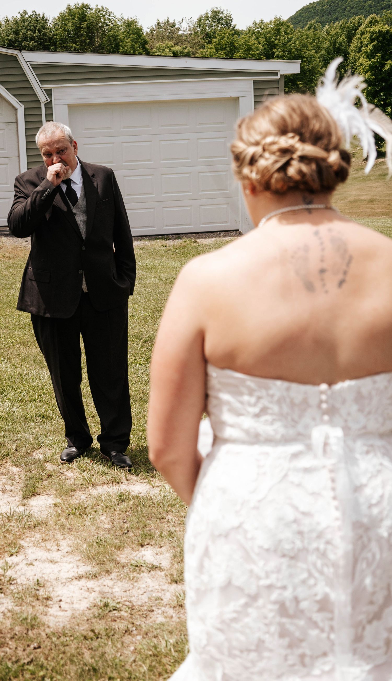 Emotional first look between a bride in white dress and someone in a suit near a garage.